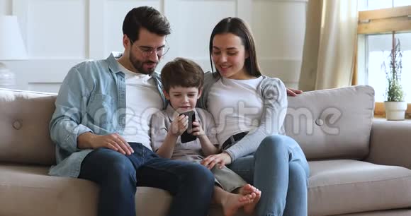 用智能手机在沙发上为孩子微笑的父母放松视频的预览图