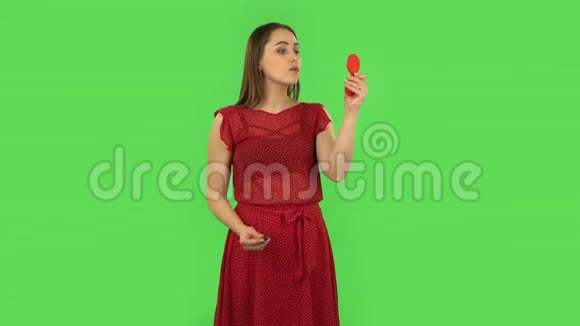 穿着红色裙子的温柔女孩正在用红色的镜子画她的嘴唇绿色屏幕视频的预览图