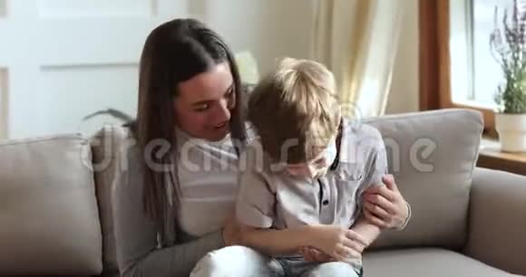 快乐的母亲挠痒可爱的孩子儿子笑着在沙发上玩耍视频的预览图