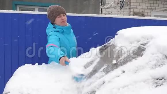 女孩从汽车玻璃上扫雪女人用刷子擦雪车从车里刮来的冰雪视频的预览图