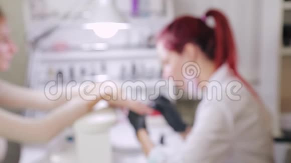 在美容院带手套的女美甲师在涂胶前先把顾客的指甲擦掉模糊翻译视频的预览图
