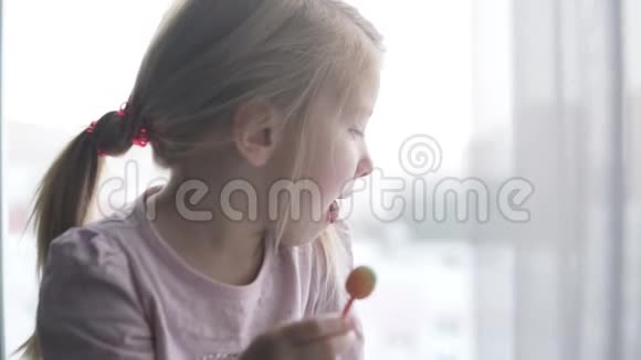 一个小女孩看着窗外在棍子上吃糖果视频的预览图