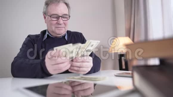 有钱的白人老人在室内清点现金的肖像微笑着戴眼镜的高级男性退休人员在视频的预览图
