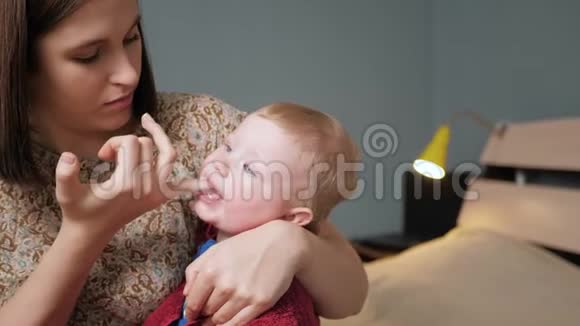 妈妈用戴在手指上的牙刷按摩器和口香糖凝胶按摩婴儿牙龈泰兴概念慢动作和中等动作视频的预览图