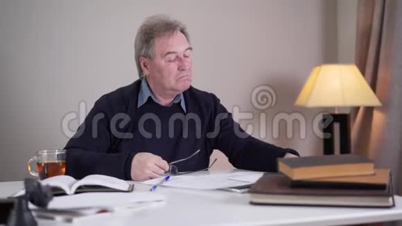 精疲力竭的高加索老人戴上眼镜和阅读文件在室内工作的高级退休人员视频的预览图