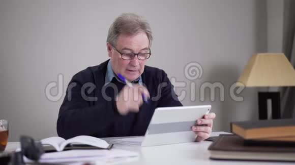 资深白种人商人滚动平板电脑屏幕和摇头成熟男人在室内上网的画像视频的预览图