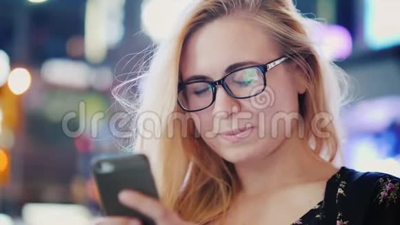 一个有魅力的年轻女人晚上在一个大城市里使用一个Smarfom围绕着广告和摩天大楼的灯光时报视频的预览图