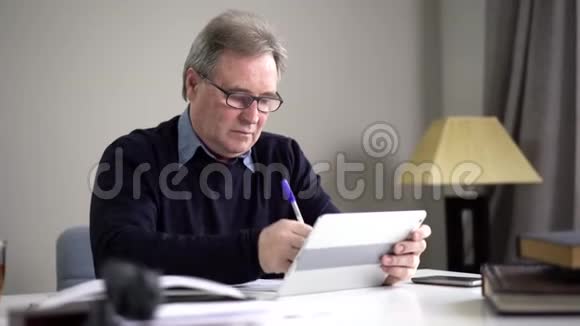 使用平板电脑和书写的戴眼镜的高加索老人的肖像严肃自信的退休人士上网视频的预览图