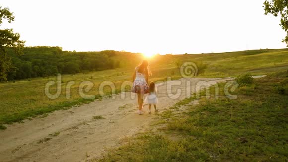 幸福的家庭观念妈妈和宝贝牵着手晚上在公园里散步在美丽的夕阳下小女儿视频的预览图