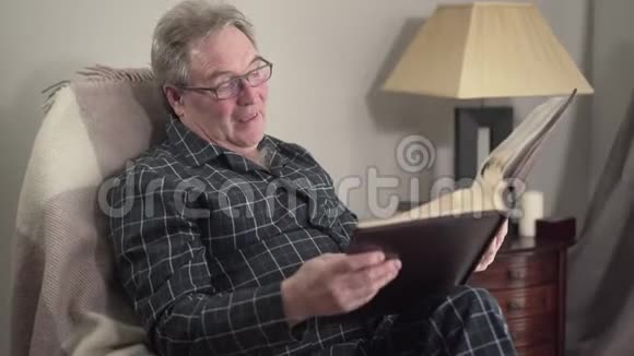 资深白种人退休人员观看相册和微笑的肖像老人回忆起晚上在家的回忆视频的预览图