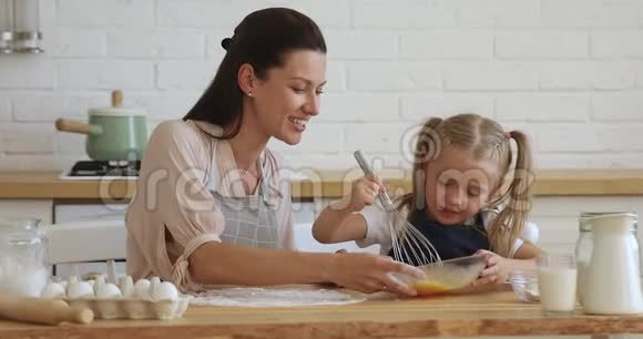 快乐的30岁的母亲看着学龄前的小女儿搅拌鸡蛋视频的预览图