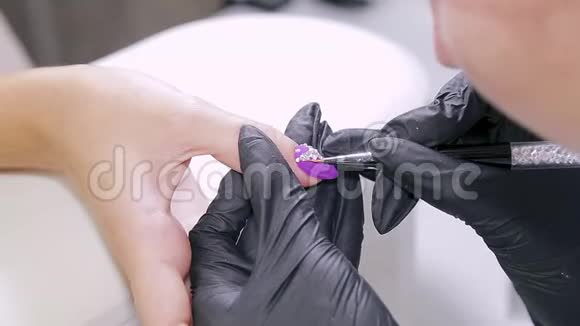 美容院的美甲师给顾客的指甲涂上带水钻的凝胶清漆视频的预览图