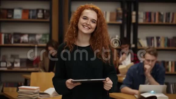 一位漂亮的长着红色头发的欧洲女学生站在高中图书馆的肖像微笑着微笑着视频的预览图