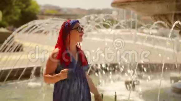 穿着蓝色裙子在公园喷泉边跳舞的快乐女人视频的预览图