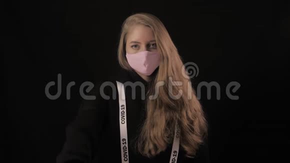 女孩戴着粉红色的面具带着铭文的丝带上面写着covid19这是一种认可的姿态孤立于黑色视频的预览图
