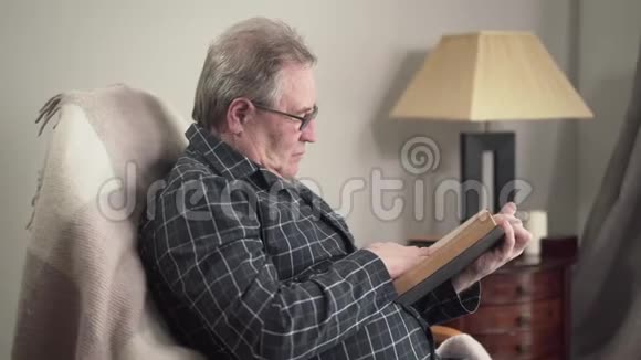 在室内阅读眼镜书的成熟白种人的侧观孤寡老人男性退休人员晚上休息视频的预览图