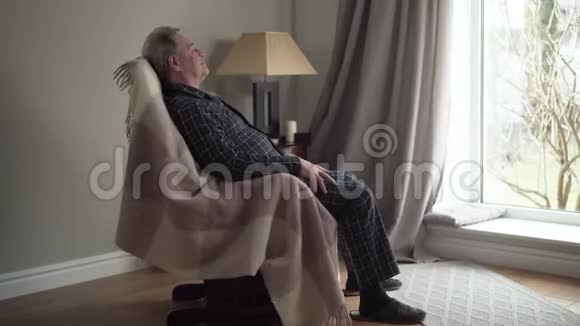 侧面观看快乐成熟的白种人在家里摇椅上摇摆微笑的高级退休人员望着窗外视频的预览图
