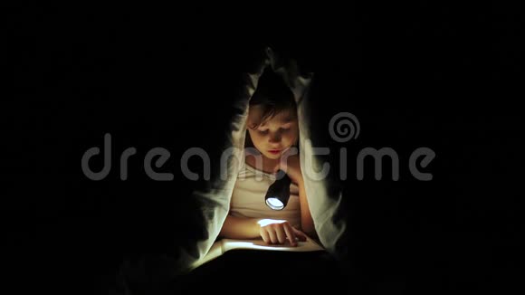 小女孩用手电筒在毯子下面读一本书视频的预览图