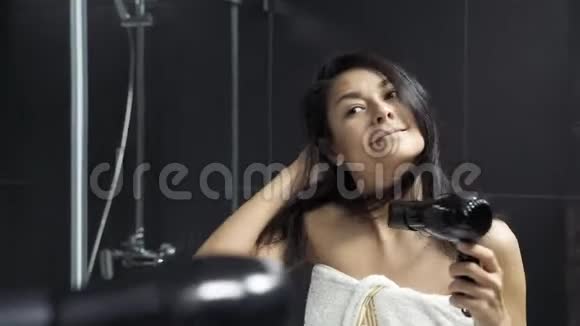 带毛巾干头发的年轻黑发女子浴室配有吹风机视频的预览图