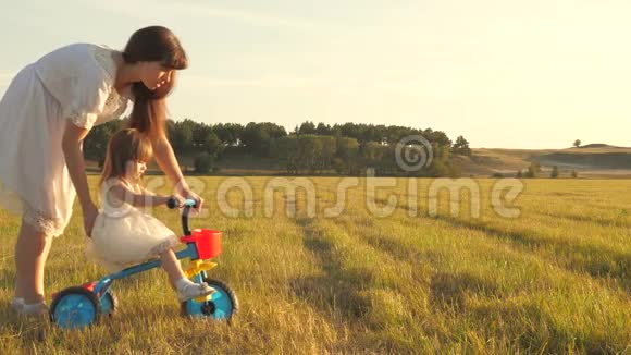 春天夏天妈妈和她的小女儿在公园里草地上玩妈妈教女儿骑自行车视频的预览图
