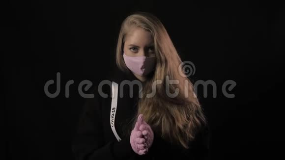女孩戴着粉红色的面具带着铭文的丝带19岁的女孩揉着她的手掌孤立在黑色背景上保健视频的预览图