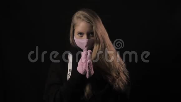 女孩戴着粉红色的面具带着铭文的丝带19岁的女孩揉着她的手掌孤立在黑色背景上保健视频的预览图