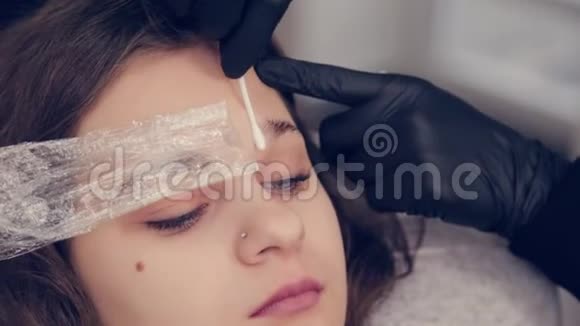 在一家美容院专业的眉毛大师将胶卷从眉毛上取下并去除眉毛上的液体视频的预览图