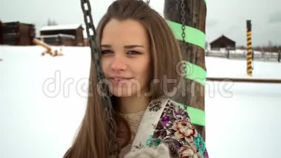 一幅长头发在秋千上摆动的少数民族女孩的肖像雪山地形慈祥的笑脸在背景中村庄和视频的预览图