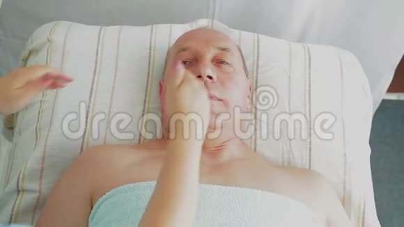 女美容师在一家水疗沙龙里给男人做一次坚定的面部按摩视频的预览图