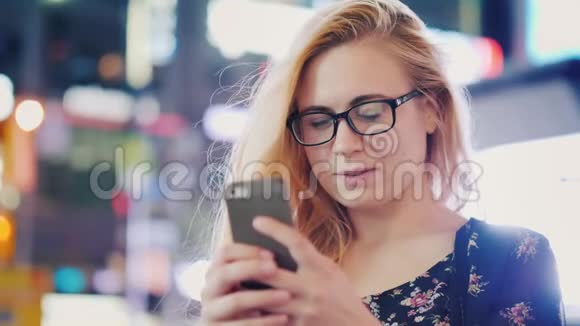 一个戴眼镜的年轻女人在夜间城市使用智能手机在夜光模糊的背景下视频的预览图