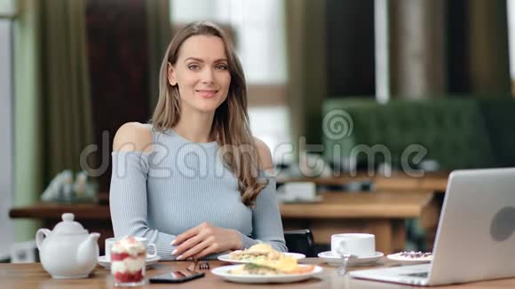 友好微笑的年轻金发女人坐在桌子上的肖像中型摄影机视频的预览图
