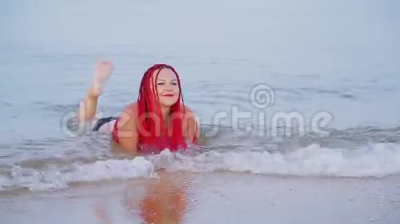 一个穿着红色辫子的黑色泳衣的女人躺在海边的海水里视频的预览图