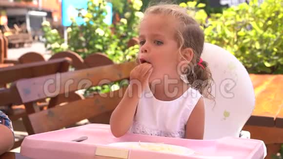 可爱的小白种人女孩在餐桌上吃意大利面坐在儿童座椅户外餐厅视频的预览图