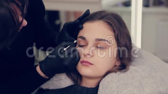 专业的女士眉师在美容院给客户处理一个带眉毛的棉芽视频的预览图