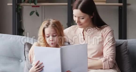可爱的女孩和妈妈坐在沙发上看书视频的预览图