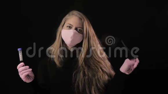 穿着粉红色面具的女孩拿着一根带血的试管上面写着covid19并扭曲了面具孤立于黑色视频的预览图