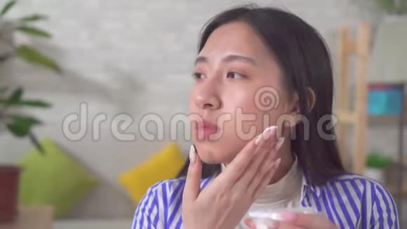 年轻漂亮的亚洲女人在家里的餐桌上使用面霜视频的预览图