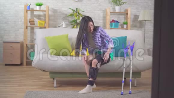 一位年轻的亚洲妇女受伤后膝盖弯曲膝盖支撑用拐杖从沙发上站起来视频的预览图