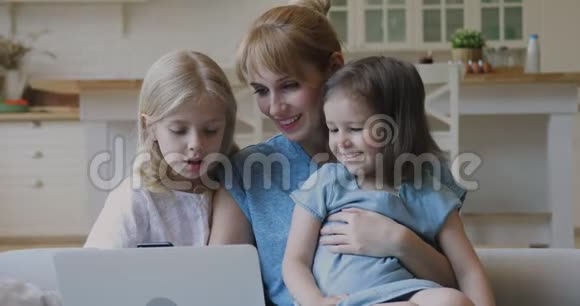 年轻的母亲拥抱着两个小女儿看着笔记本电脑屏幕视频的预览图