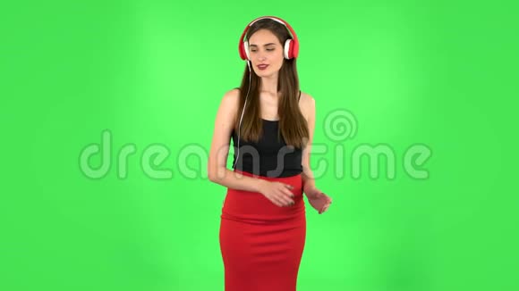 快乐的女孩跳舞享受音乐在大红色耳机绿色屏幕视频的预览图