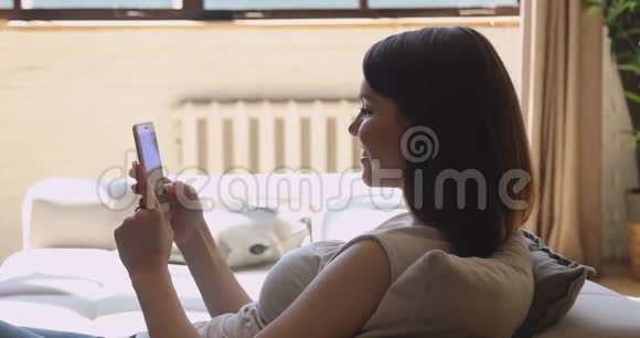 年轻迷人的女人躺在舒适的沙发上在线聊天视频的预览图