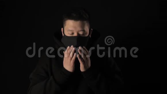 戴着黑色医学面具的亚裔男子戴着白色胶带在黑色背景下咳嗽视频的预览图