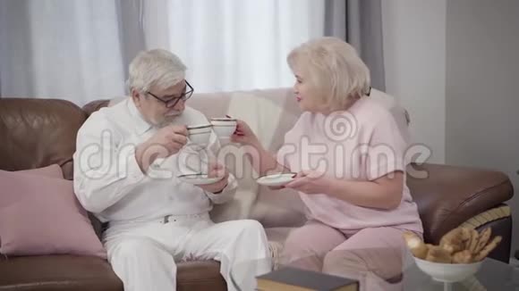 开朗的老白种人夫妇碰着茶杯说话快乐成熟的退休者在家里度过空闲时间视频的预览图