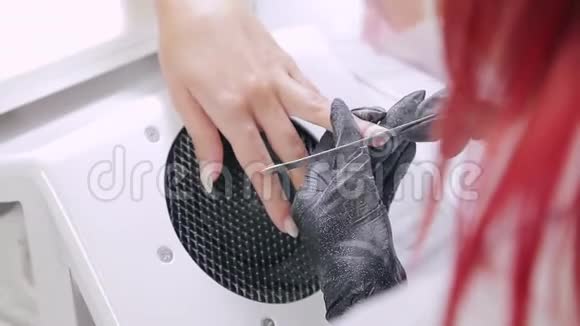 美容店里戴着手套的美甲女士在涂胶前用指甲锉钉给客户指甲视频的预览图