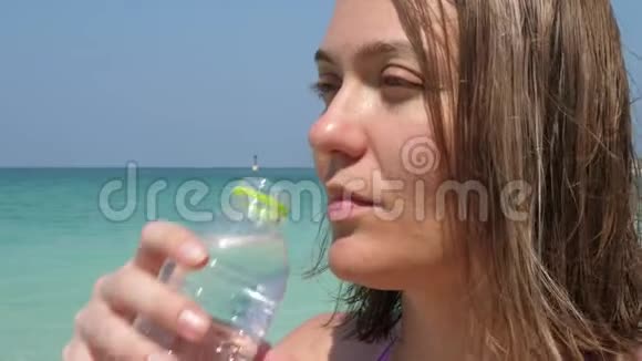 有魅力的女人在海滩的瓶子里喝饮料水视频的预览图