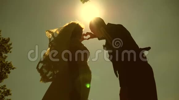 一对相爱的夫妇的剪影用他们的手在地平线上的太阳对面做一个心的象征太阳在手视频的预览图