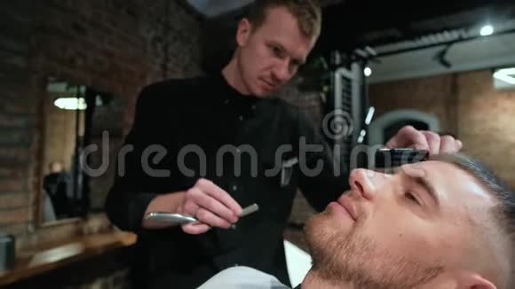 英俊的年轻人在理发店刮胡子胡子用直剃刀在特写专业人员视频的预览图