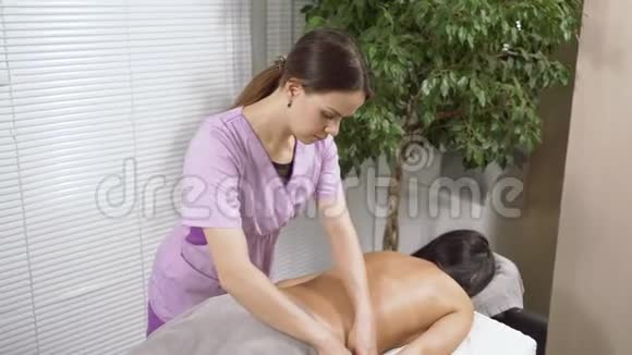 女按摩师在医疗办公室给一个年轻的黑发女人做背部按摩视频的预览图