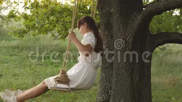 飞行的梦想自由女孩在阳光下在橡木树枝上荡秋千快乐的童年概念一个漂亮的女孩视频的预览图
