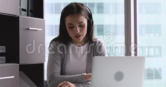 戴着耳机在办公室在线学习的积极女性视频的预览图
